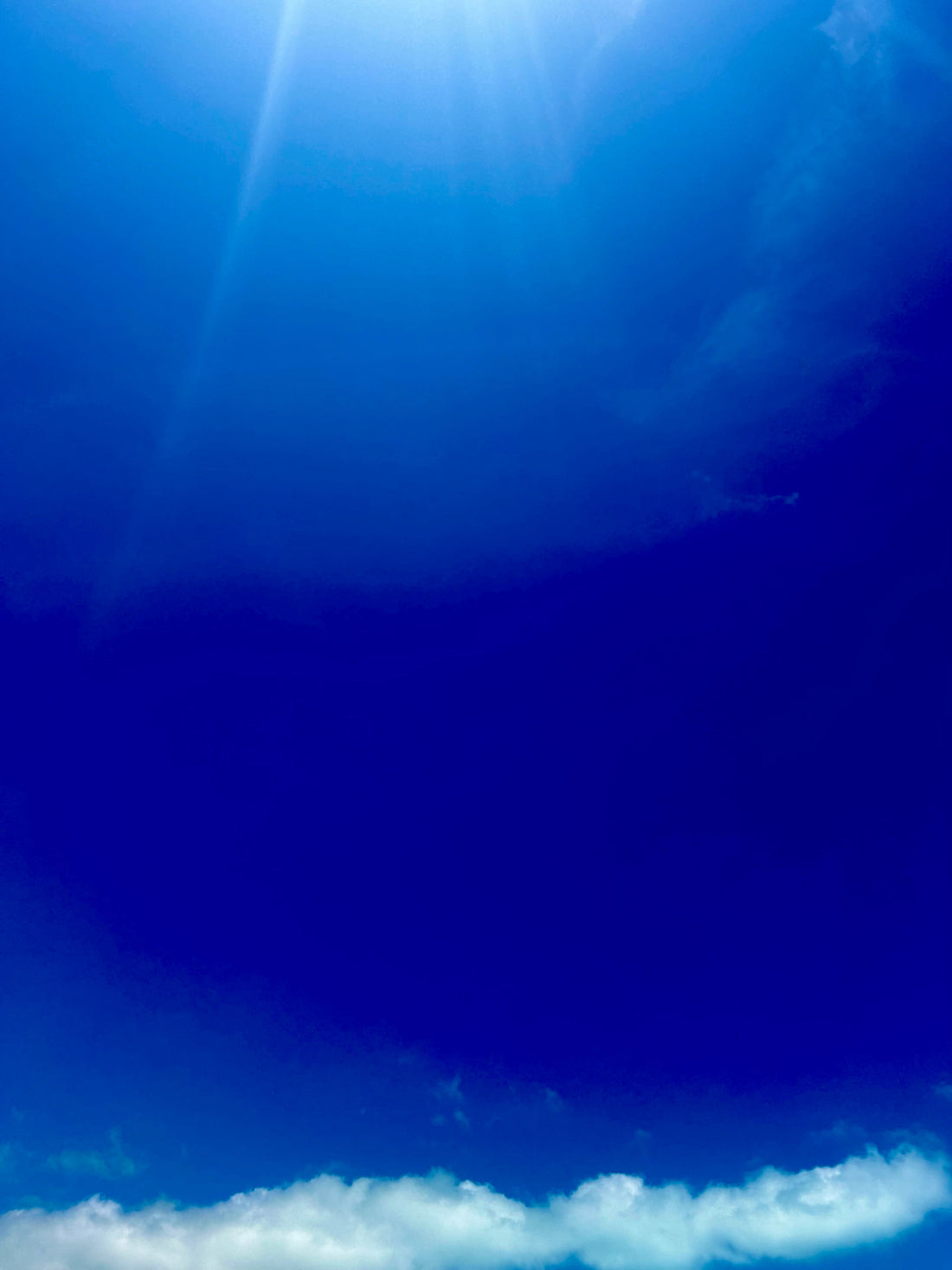deep blue sky with sun beaming through clouds