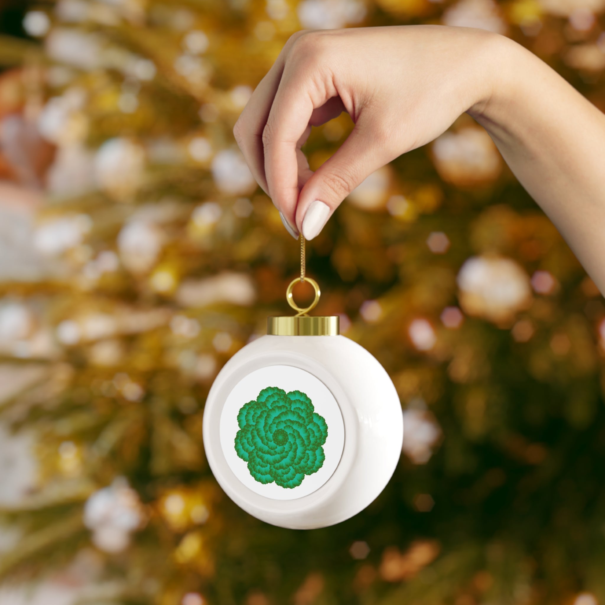 White ornament with green pattern held by a hand against a blurred Christmas tree background